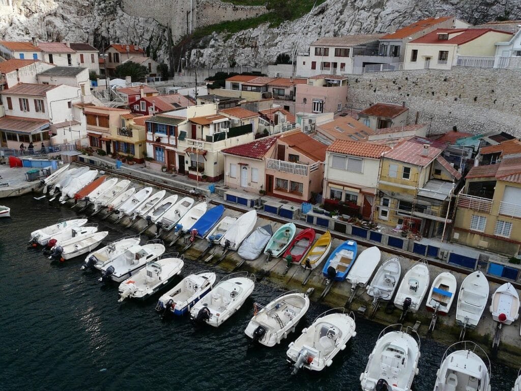 Colourful fishing boats moored in the Vallon des Auffes, with small waterfront restaurants and the arched bridge in the background.